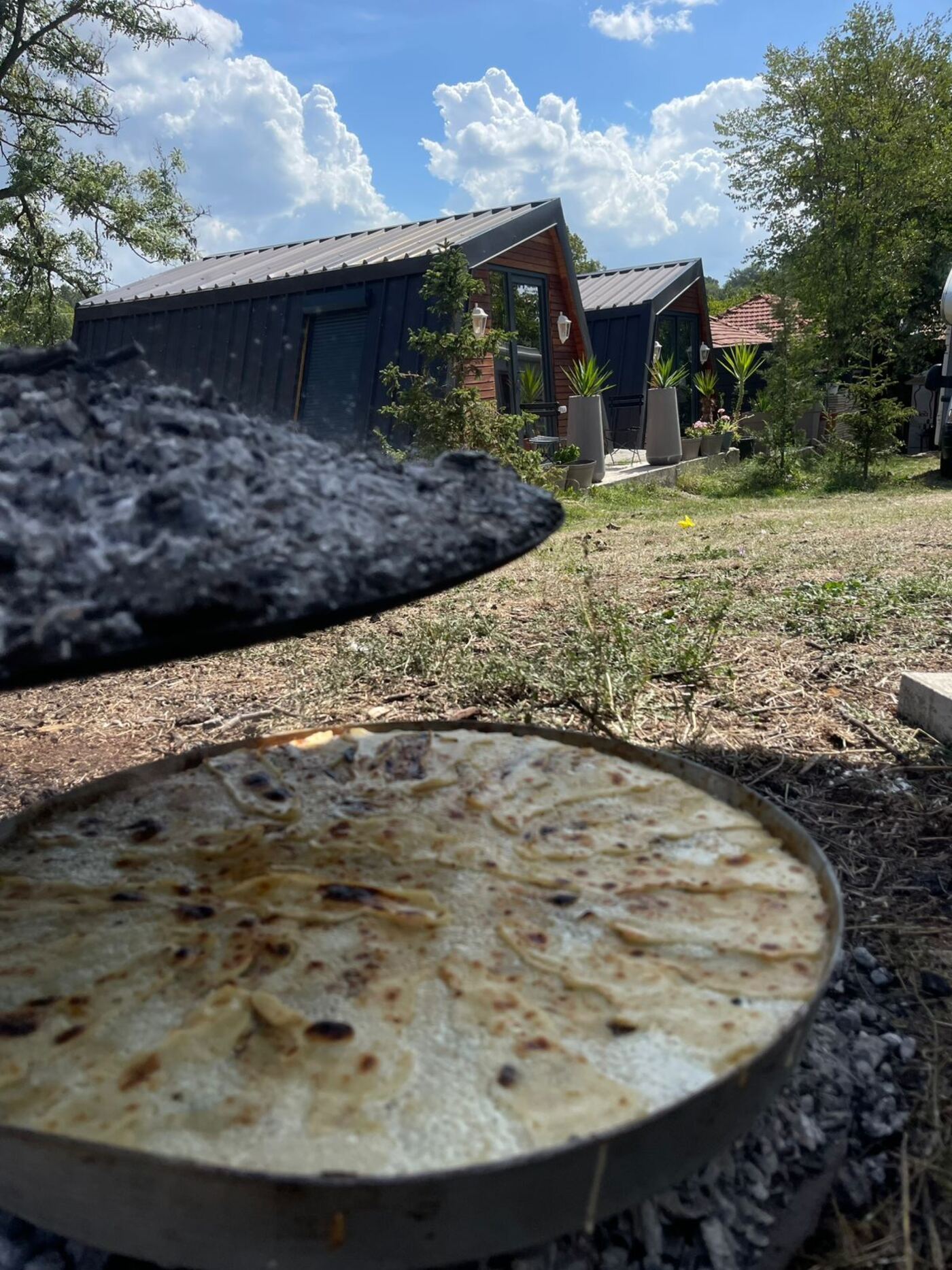 Homemade flatbread cooking over the fire at Teddy Camp campground, Kosovo, bungalows in the background