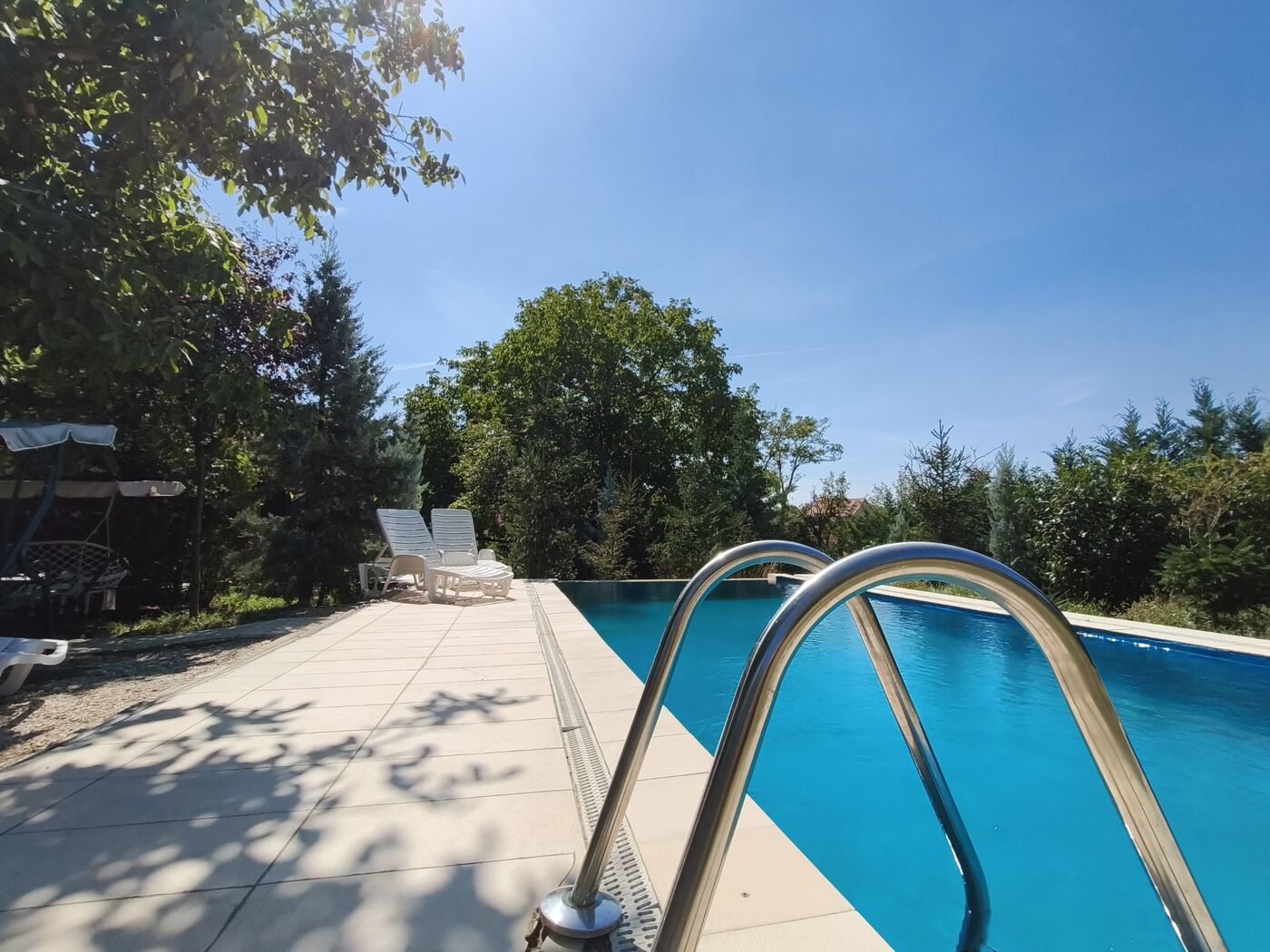 Sunny poolside view with steel ladder and loungers at Teddy Camp